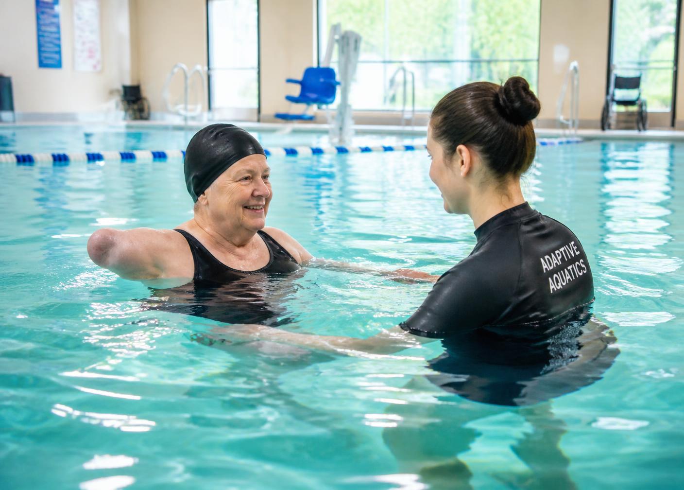An adaptive aquatics instructor working with an older swimmer in an indoor pool